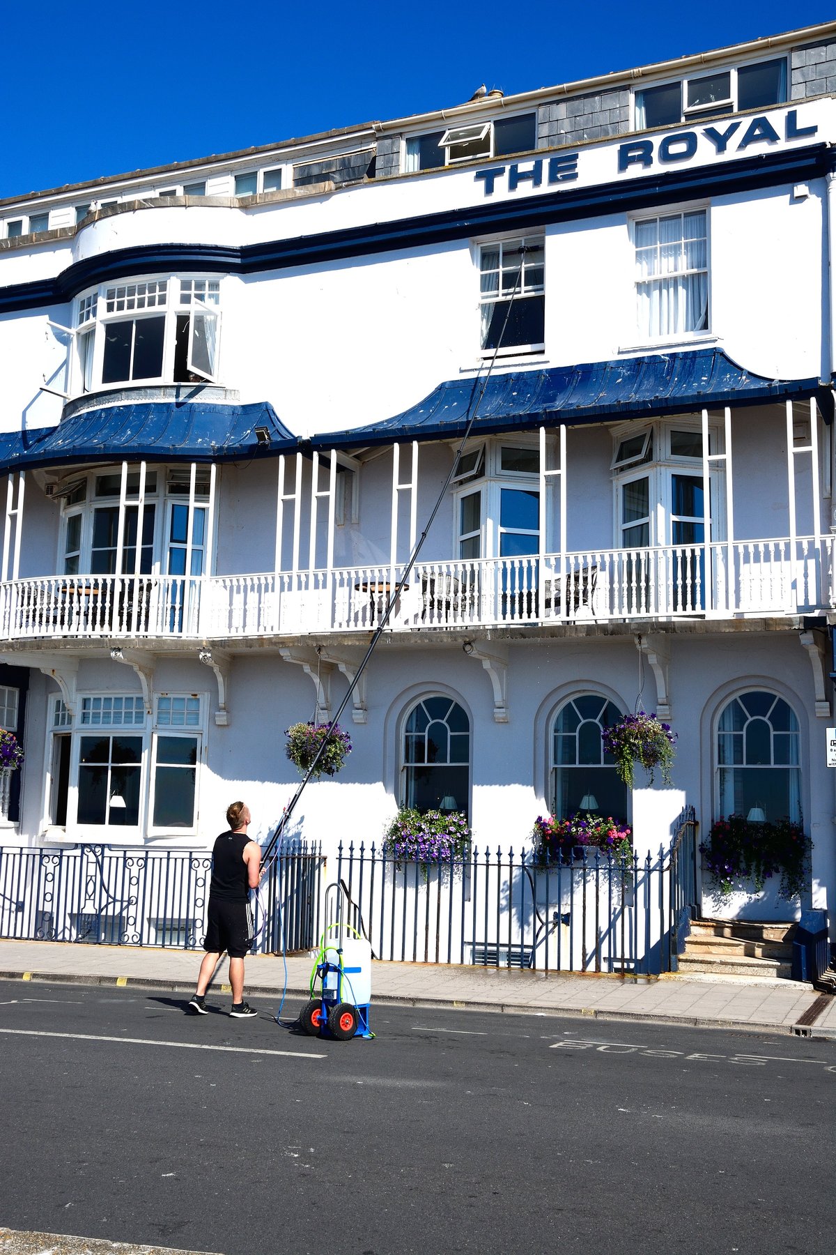 Window cleaner cleaning upstairs windows on the front of The Royal York and Faulkner Hotel, Sidmouth, Devon, UK, Europe.