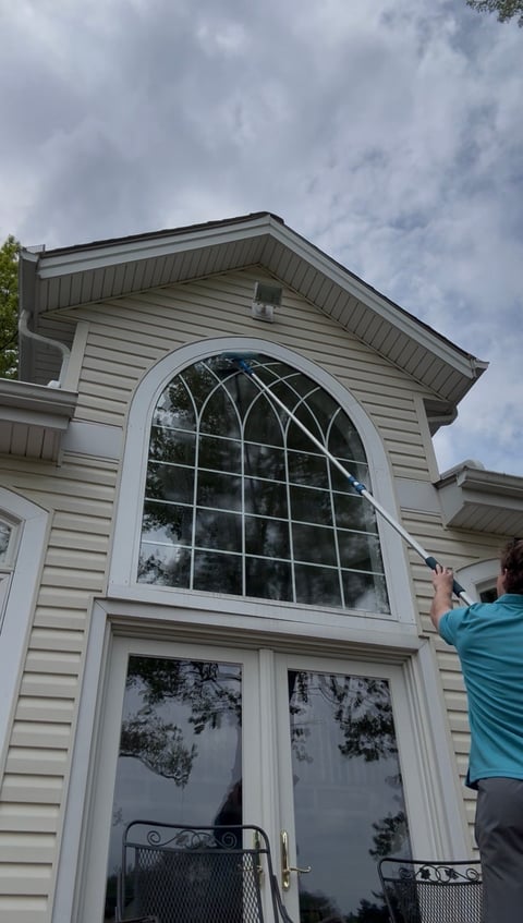 Beige house exterior with large arched window above glass double doors, person in turquoise shirt visible on right side