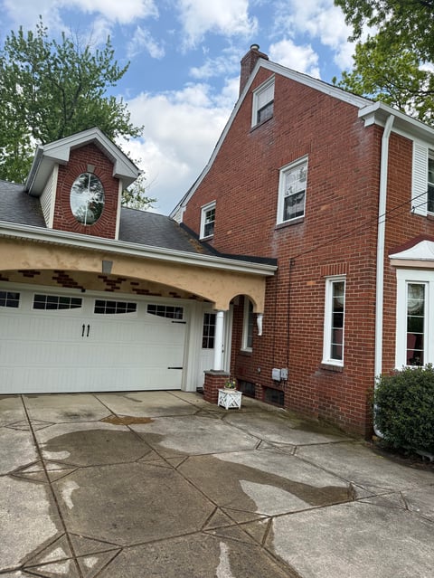 Red brick colonial-style house with white trim, two-car garage, and manicured landscaping on a sunny day