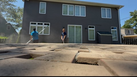 Modern gray two-story house with two people standing on a cracked concrete driveway in sunny weather