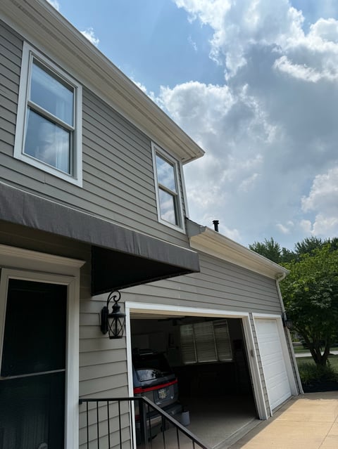 Modern gray two-story house with garage open, white trim, and green lawn visible under clear blue sky with clouds